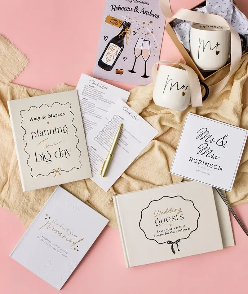Wedding-themed stationery and gift set with planning book, guest book, Mr and Mrs mugs, and congratulations card on a soft pink background